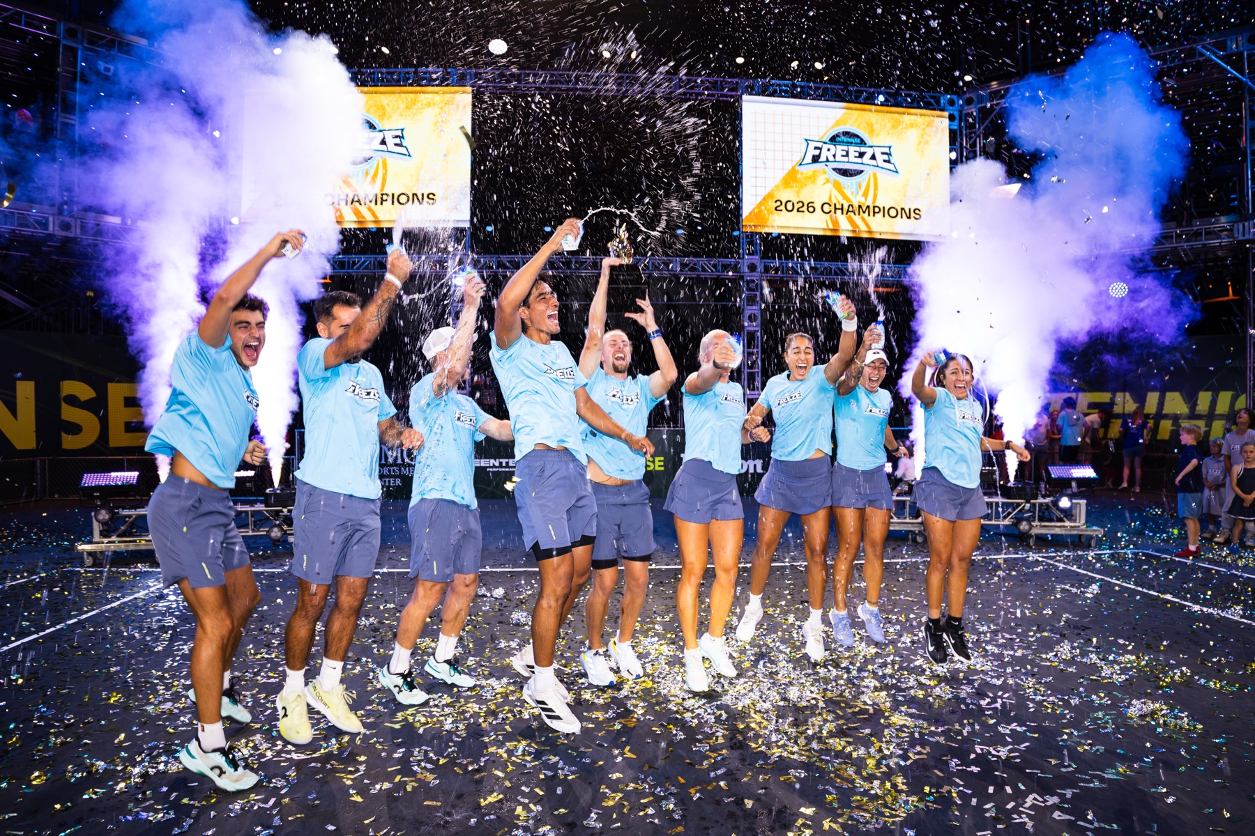Freeze players jumping and spraying champagne under confetti, beneath banners reading Freeze 2026 Champions.