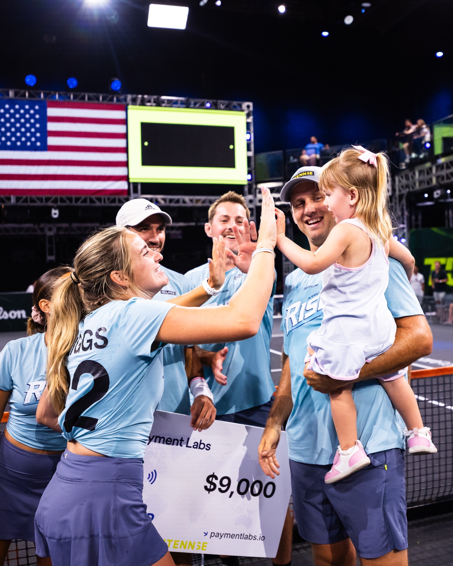 A Rise player high-fiving a small girl held in a teammate&rsquo;s arms, the team smiling around them.